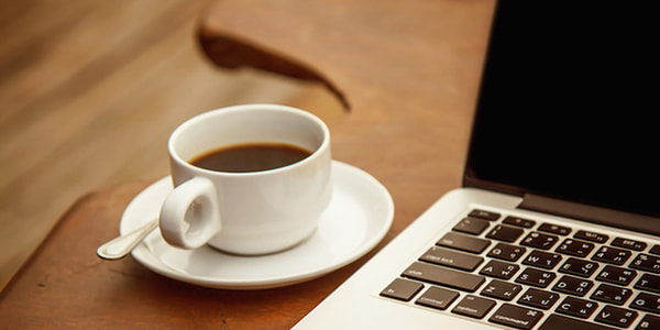 Black coffee in a white cup on a table with a computer.